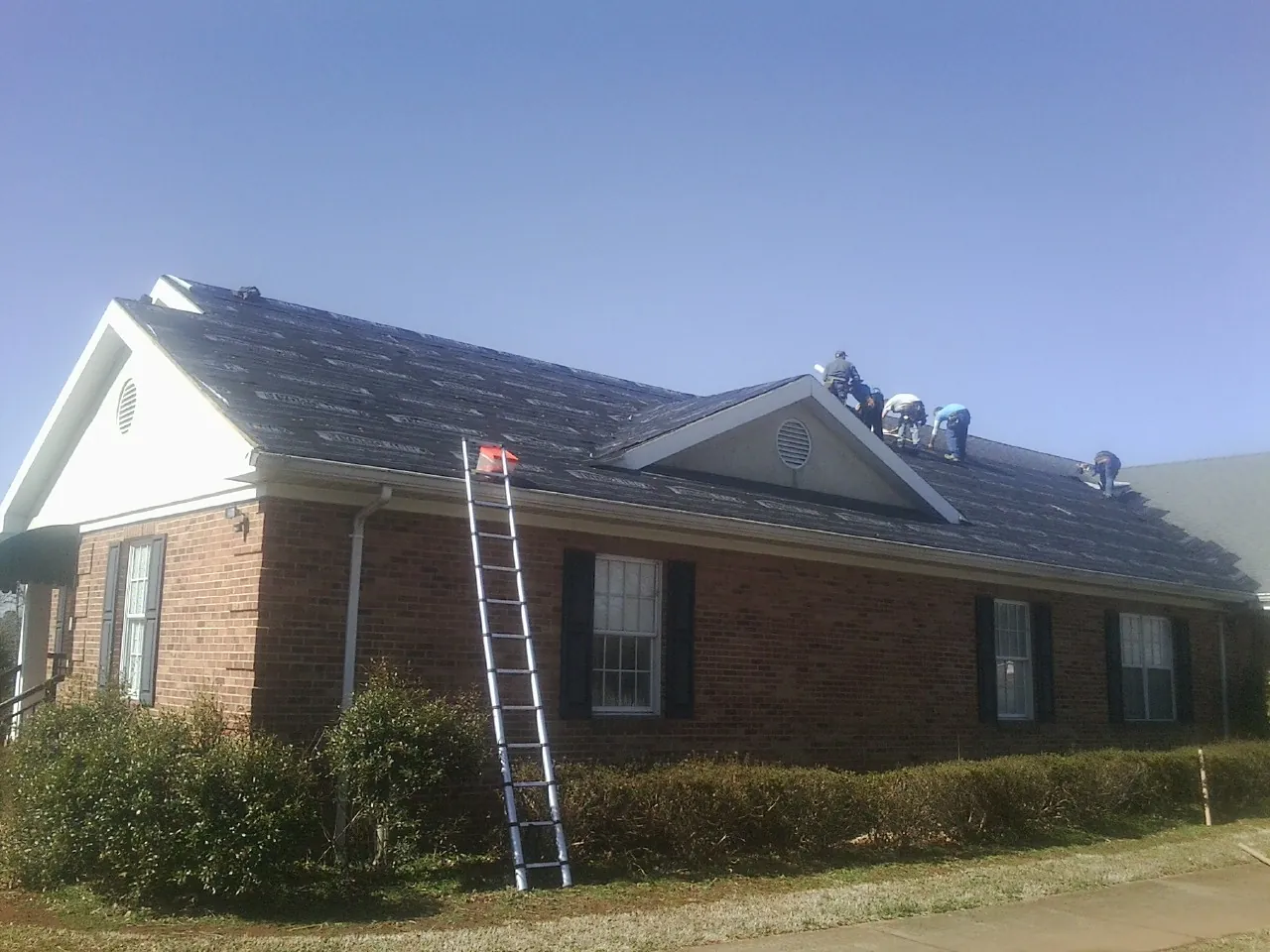 Crew tearing shingles off a brick ranch roof with a ladder set — Emergency Roof Repair work by our crew in Villas