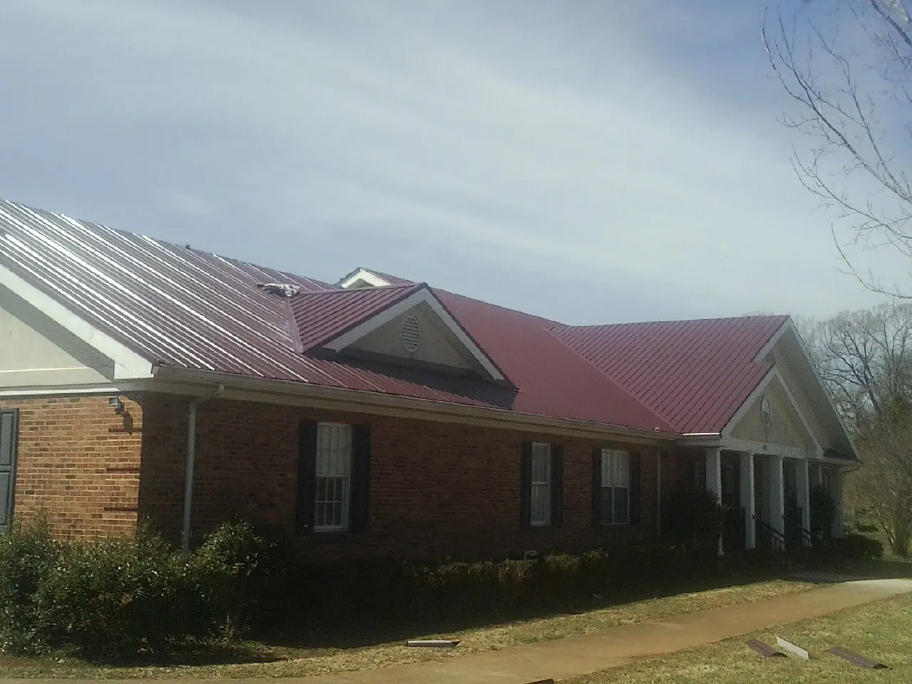 Red metal roof with gabled entries on a long brick building, from a Hail Damage Roof Repair job in Villas
