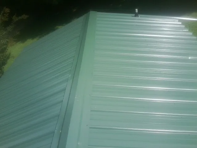 New green metal panels meeting at the ridge of a roof — Flat Roof Repair work by our crew in Villas