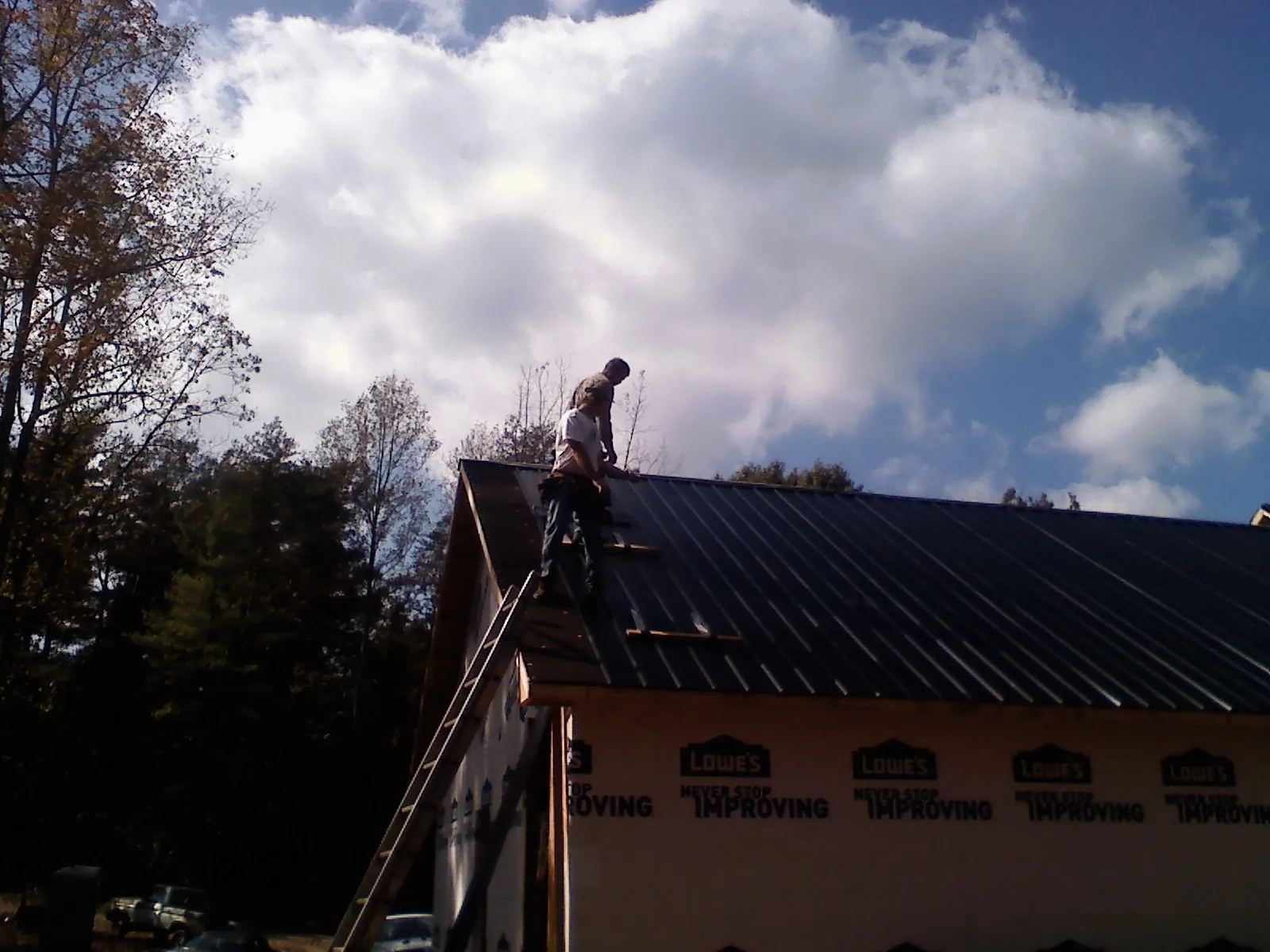 Roofer fastening dark metal panels high against a cloudy sky, from a Roof Inspection job in Villas