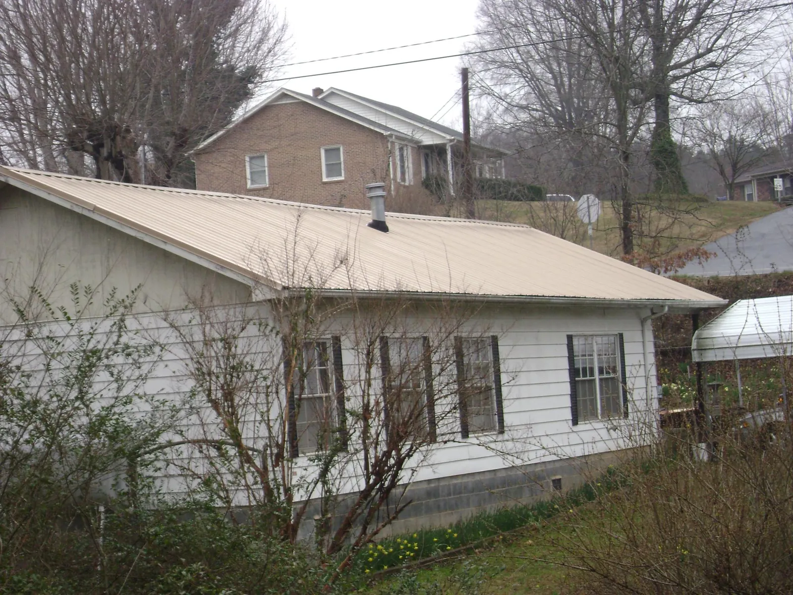 Tan metal roof on a white sided house set into a hillside — Commercial Roofing by Roofing Brothers in Villas