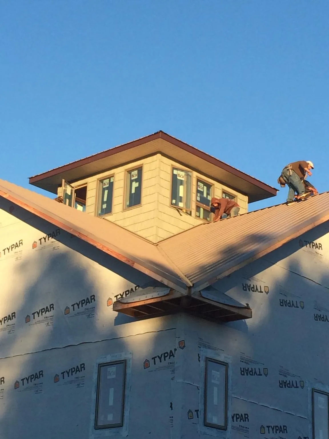 Roofers working around a rooftop cupola on a new metal roof at sunset — Roof Waterproofing in Villas by Roofing Brothers